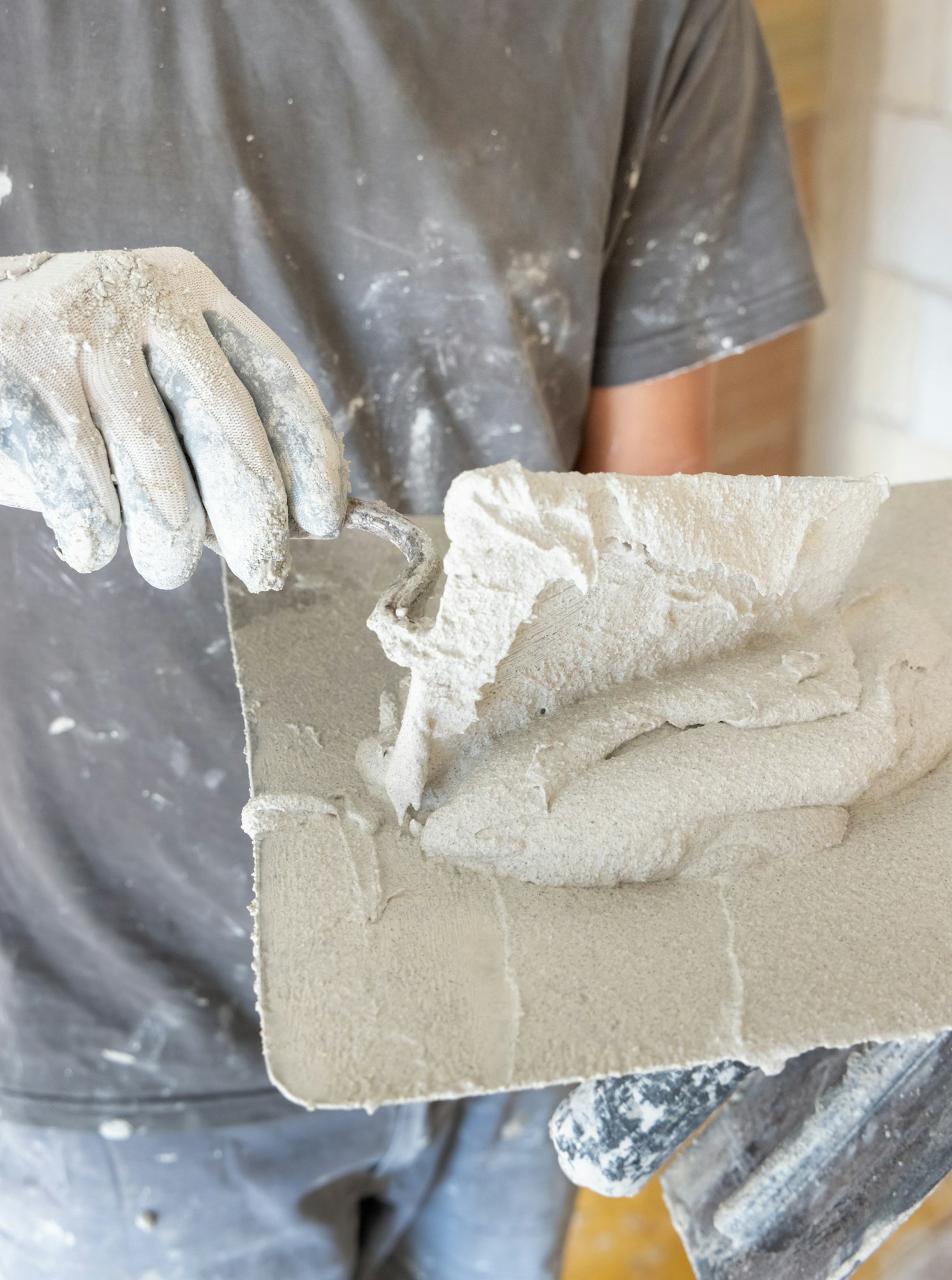 Craftsman in dirty gloves puts plaster, mortar or cement on a metal trowel. Men in a gray shirt